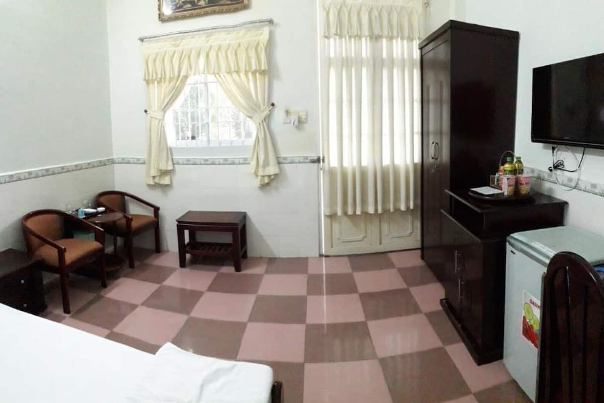 A hotel room with a bed, a desk, two chairs, a small table, a wardrobe, a television, and a window with curtains.