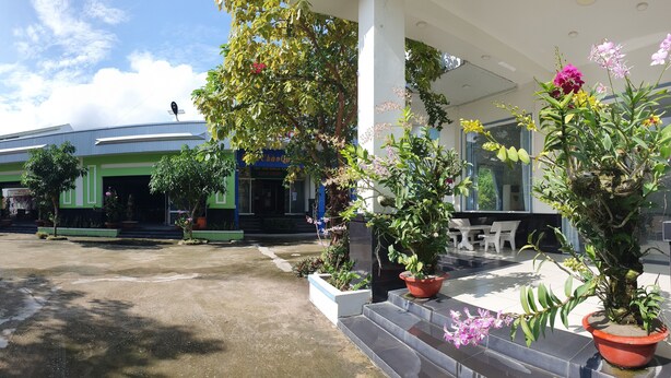 A hotel entrance with a green and white facade, outdoor seating, and potted plants. - Ngoc Han Hotel (Thoi Son)