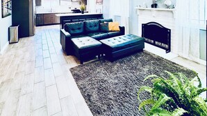 Een moderne woonkamer met een modulaire bank, een open haard en een keuken op de achtergrond.