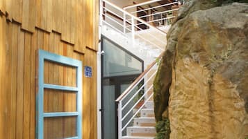A staircase leading to a wooden door with a blue frame, surrounded by potted plants and a large rock.