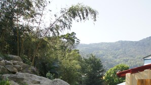 Eine Treppe führt zu einer Terrasse mit Blick auf eine gebirgige Landschaft, umgeben von viel Grün und Felsen.