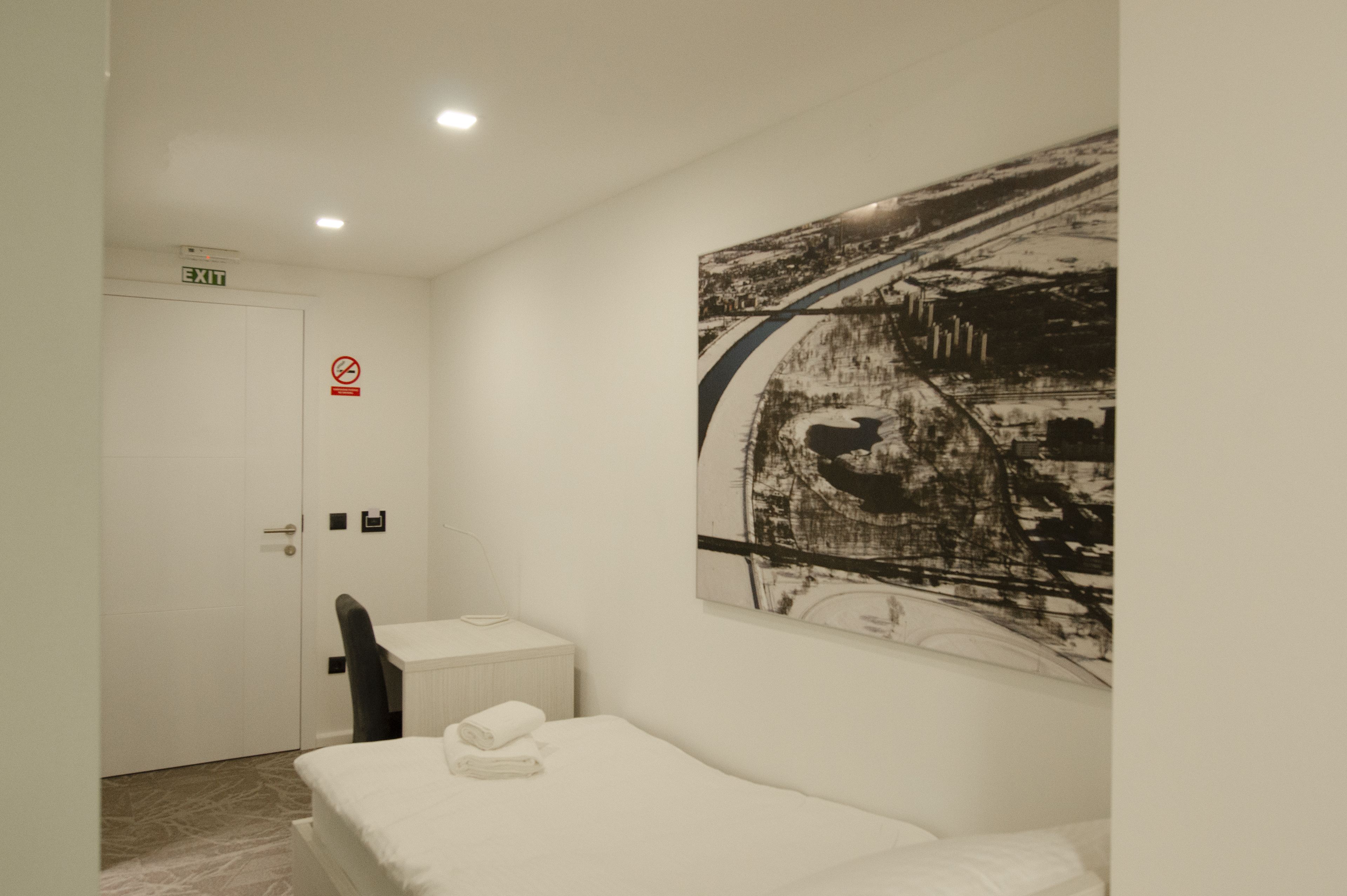 Una habitación de hotel con cama, una silla, un escritorio y un cuadro colgado en la pared.