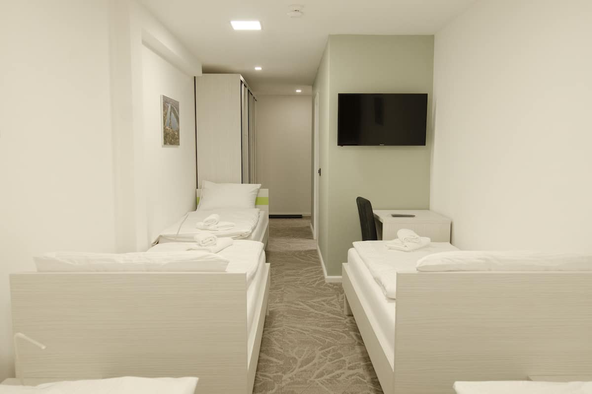 A hotel room with two single beds, a desk, a chair, a flat-screen TV, and a wardrobe.