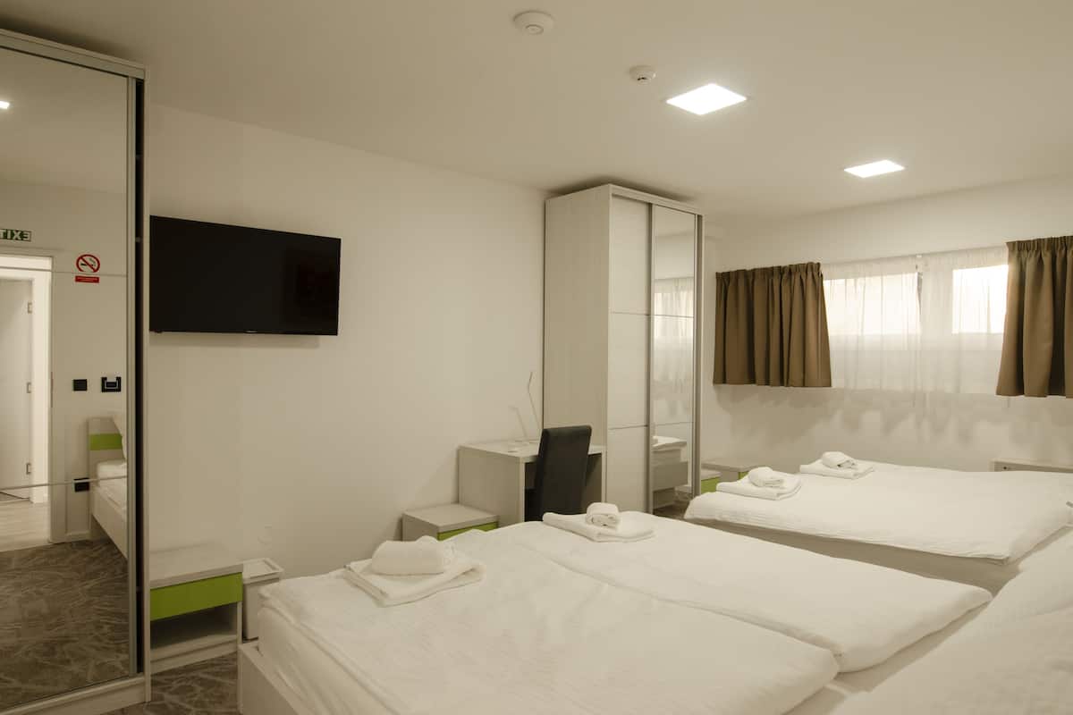A hotel room with two beds, a TV, a mirror, a desk, and a bathroom.