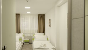 Ein Hotelzimmer mit zwei Einzelbetten, einem kleinen Tisch, einem Stuhl, einem Fenster mit Vorhängen und einer Tür.