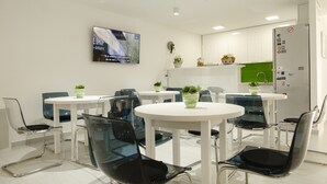 Ein moderner Essbereich mit runden Tischen und Stühlen, einem flachbildfernseher an der Wand und einem Kühlschrank mit Magneten.