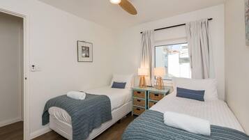 Two single beds with matching bedding, a ceiling fan, and a window with curtains.