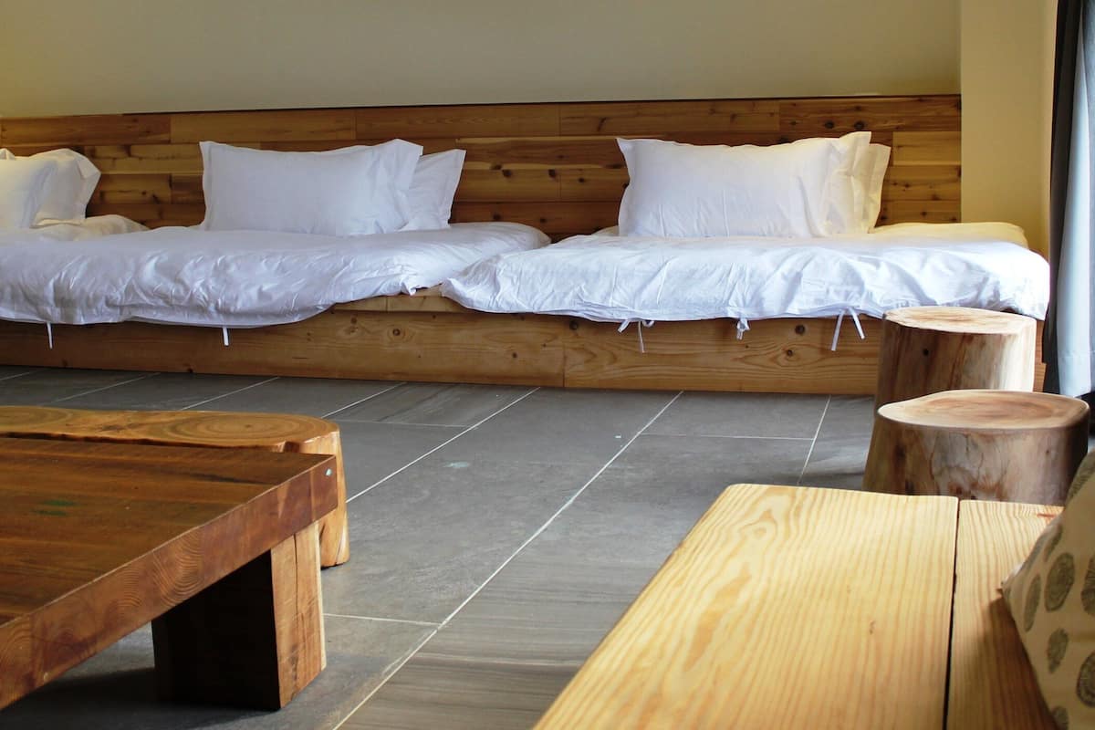 Une pièce avec un lit en bois, une table en bois et un tabouret rond en bois.
