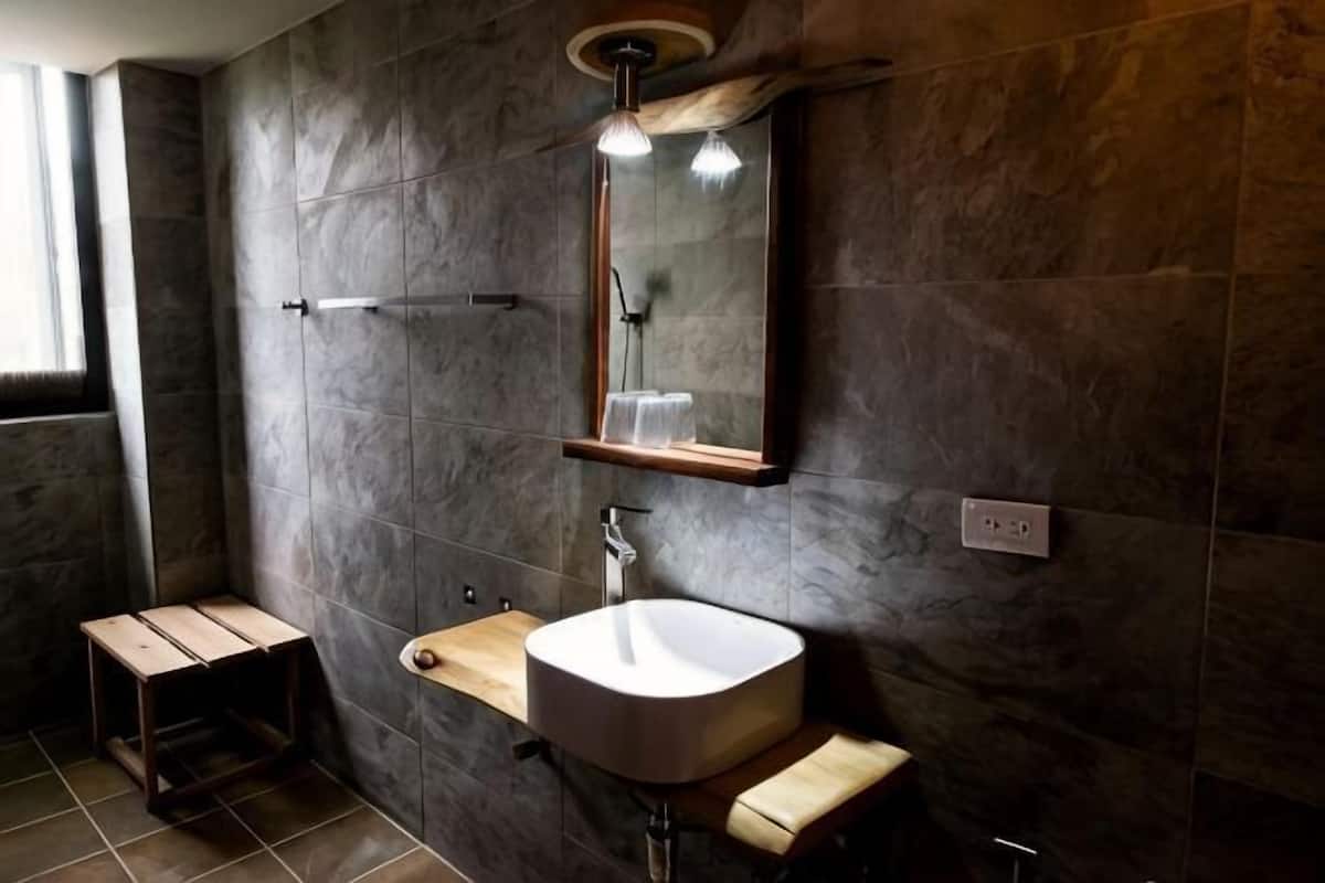 Une salle de bain avec un mur en pierre, une étagère en bois, un lavabo et un miroir.