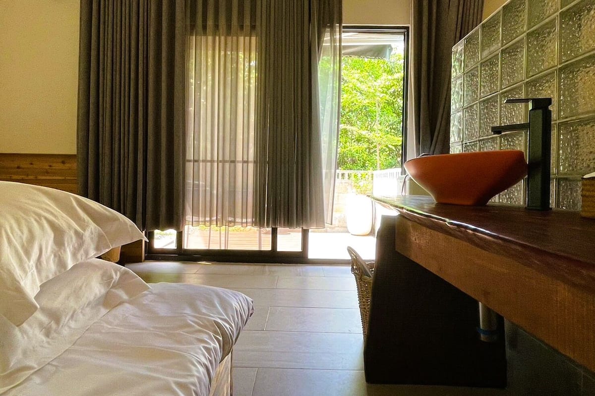 Une chambre d’hôtel avec un lit, un bureau sur lequel se trouve un bol, et une vue sur la verdure par la fenêtre.