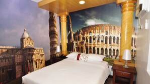 A hotel room with a large bed, a nightstand with a lamp, and a mural of famous landmarks. - Seascape Resort (Bauan)