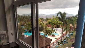 A view from a hotel room window overlooking a pool area with a wooden deck, outdoor seating, and a distant body of water. - Seascape Resort (Bauan)