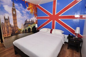 Un dormitorio con un gran mural de monumentos de Londres, una cama con ropa de cama blanca y una mesita de noche con una lámpara.