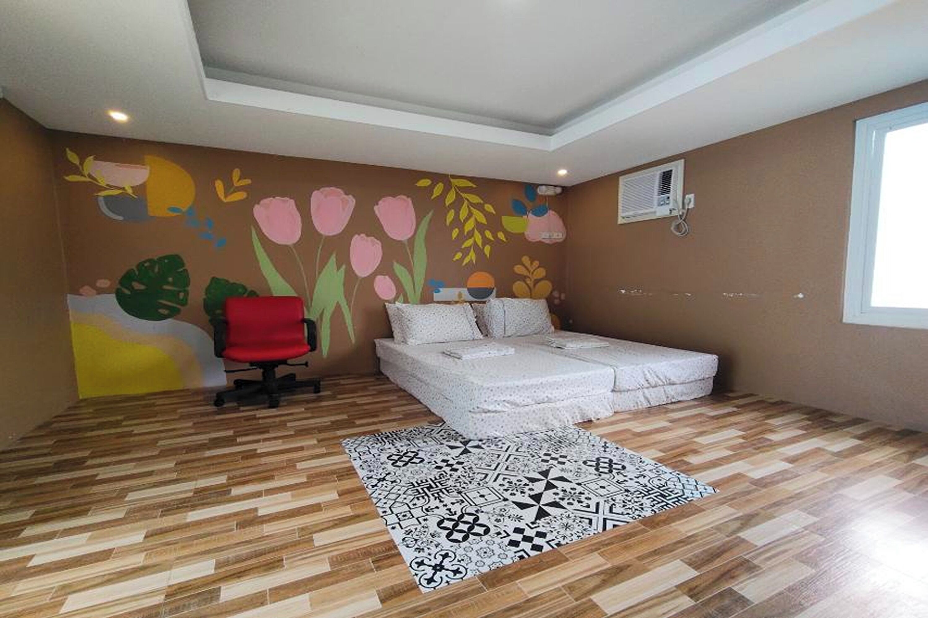 A bedroom with a bed, a chair, a patterned rug, and a wall mural.