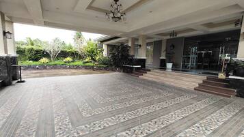 A spacious outdoor area with a patterned tile floor, a staircase leading to a covered entrance, and a view of the surrounding greenery.