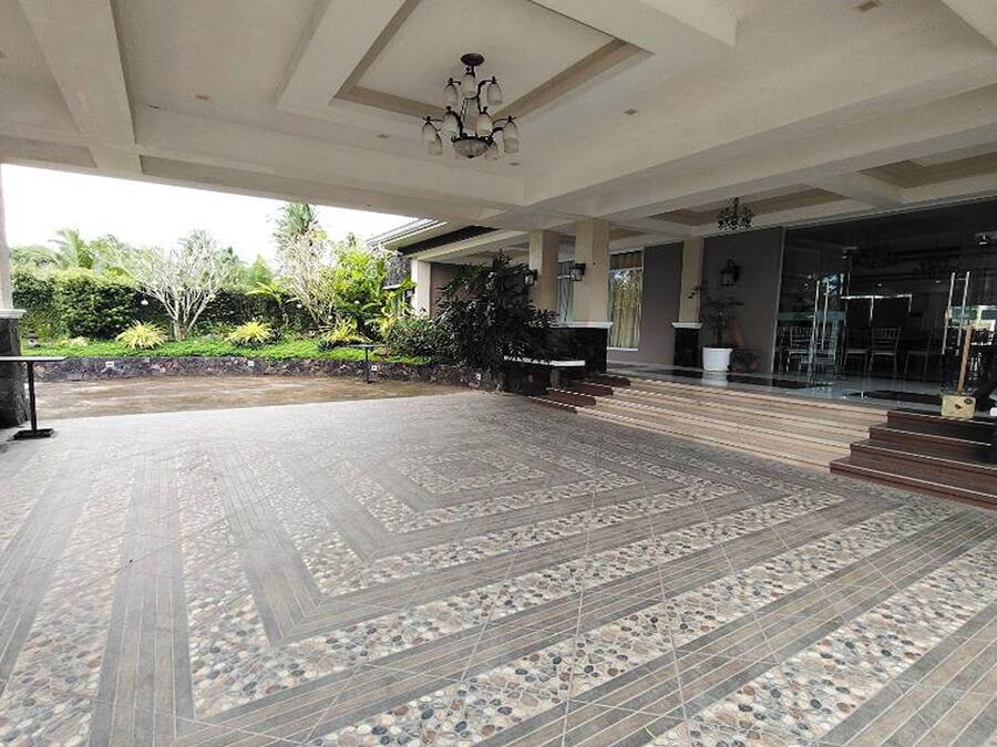 A spacious outdoor area with a patterned tile floor, a staircase leading to a covered entrance, and a view of the surrounding greenery.