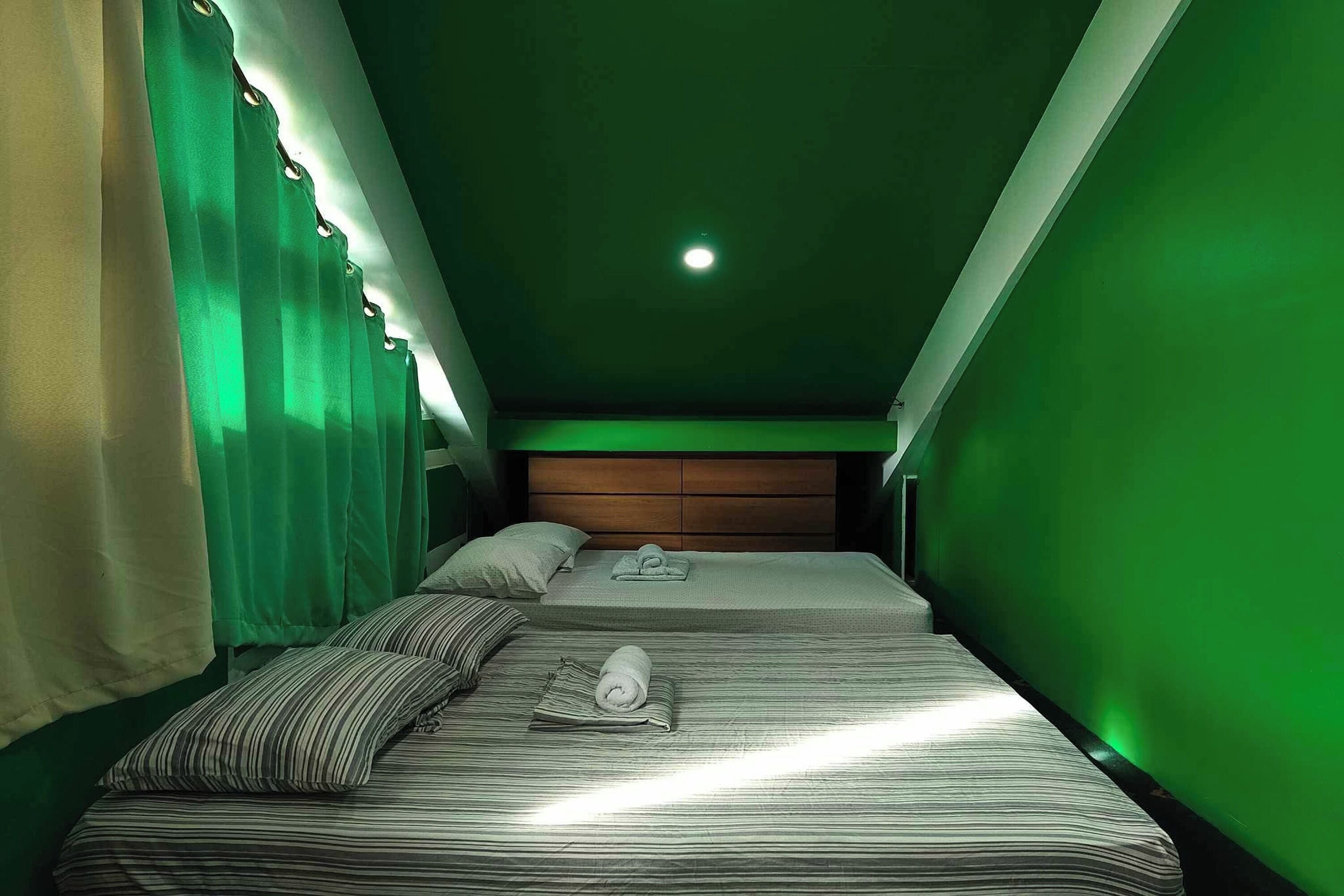 A room with two beds, a wooden headboard, and a green wall.