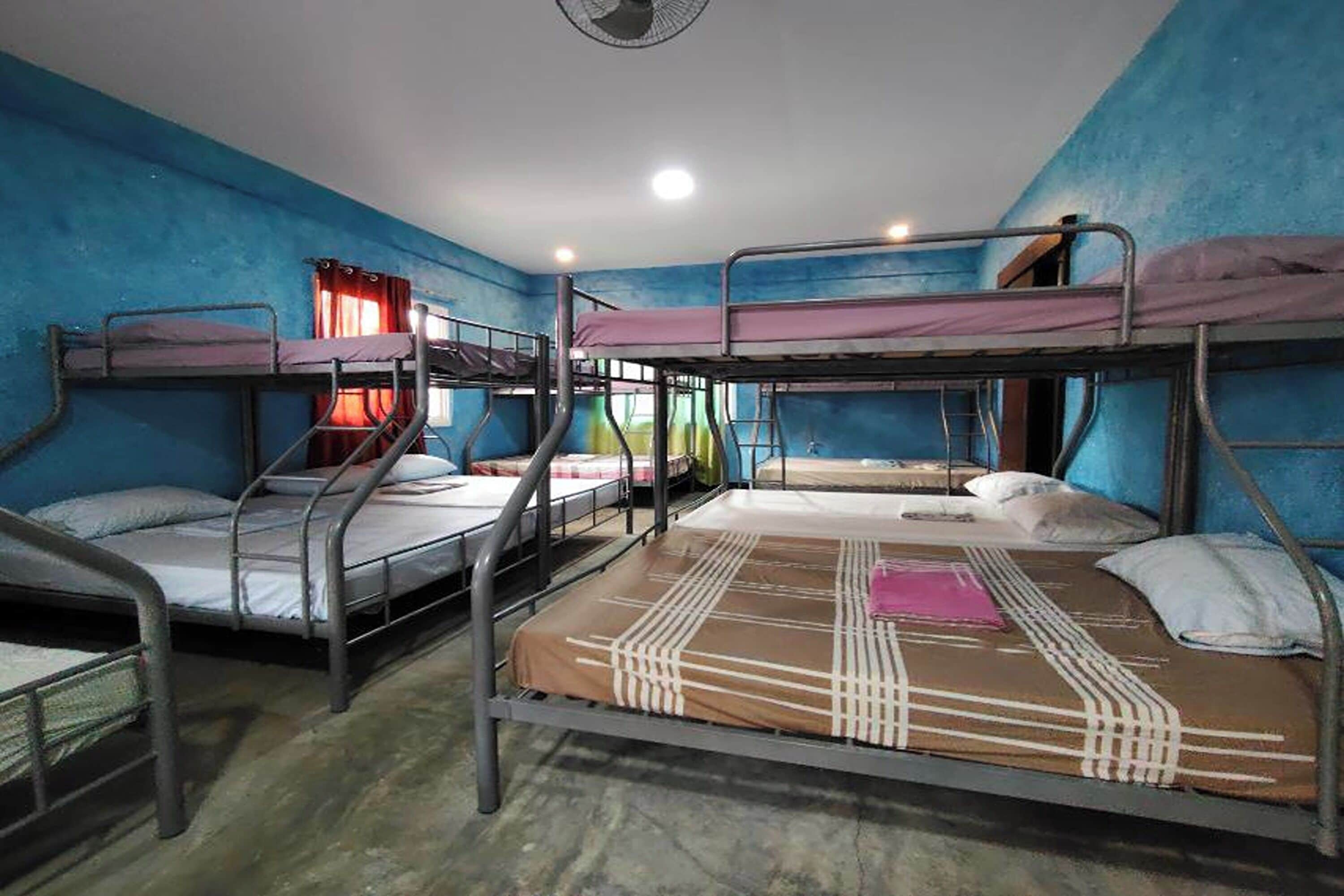 A dormitory room with bunk beds, a ceiling fan, and a window with red curtains.
