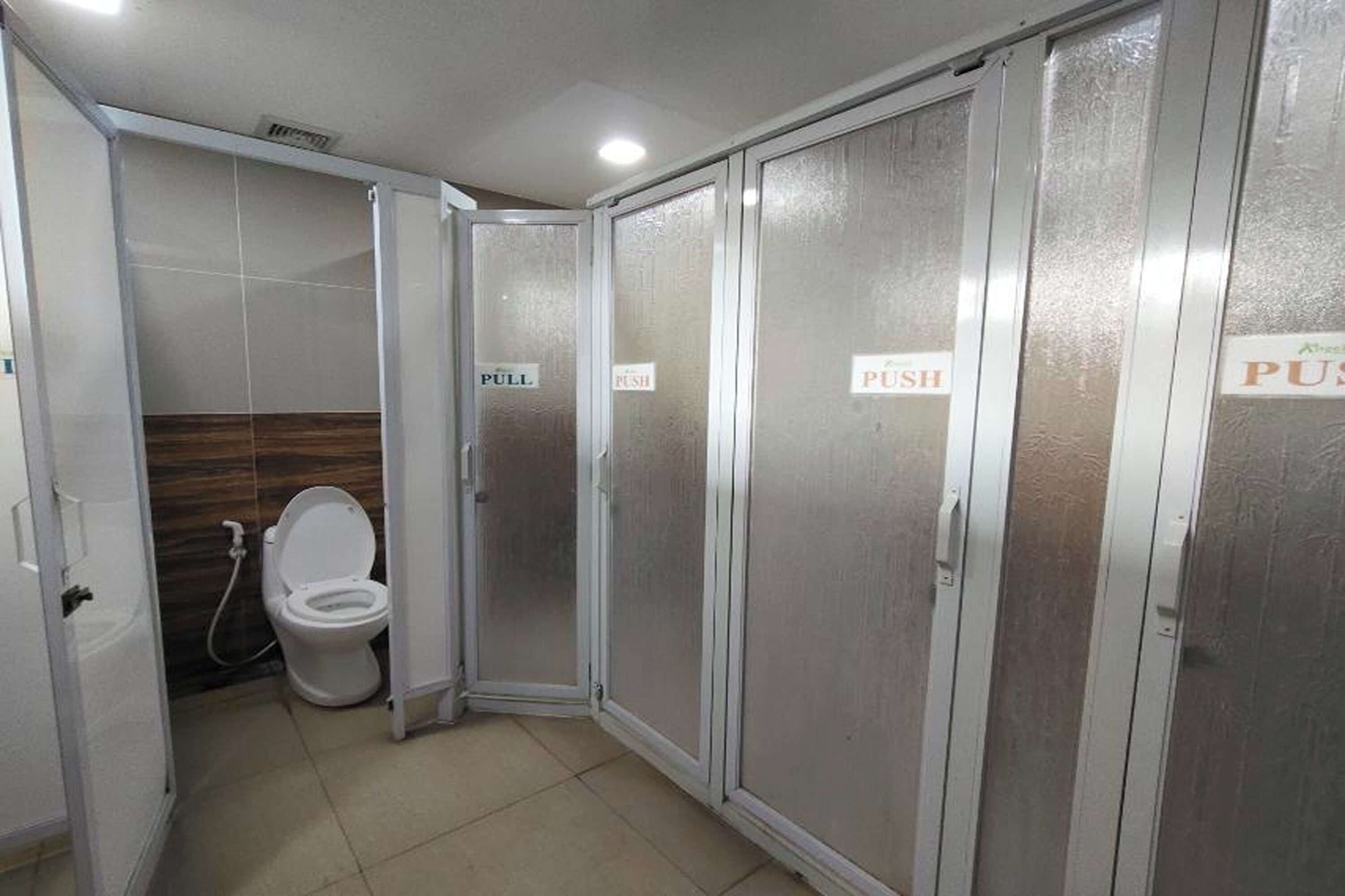 Ein Badezimmer mit Toilette, Dusche und Milchglas-Türen, auf denen 'ÖFFNEN' und 'ZIEHEN' stehen.