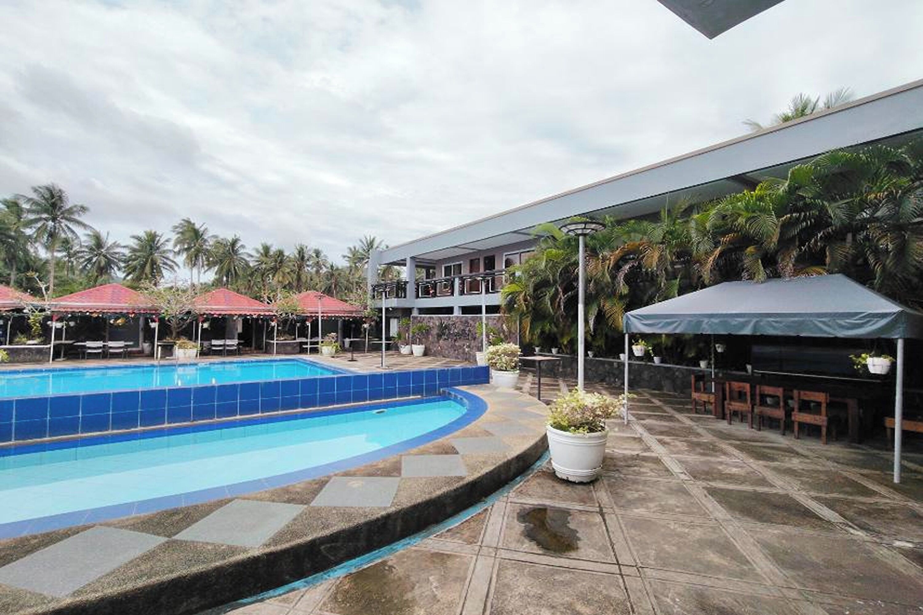 Una piscina de borde curvo, rodeada por un patio con mobiliario exterior y sombrillas.