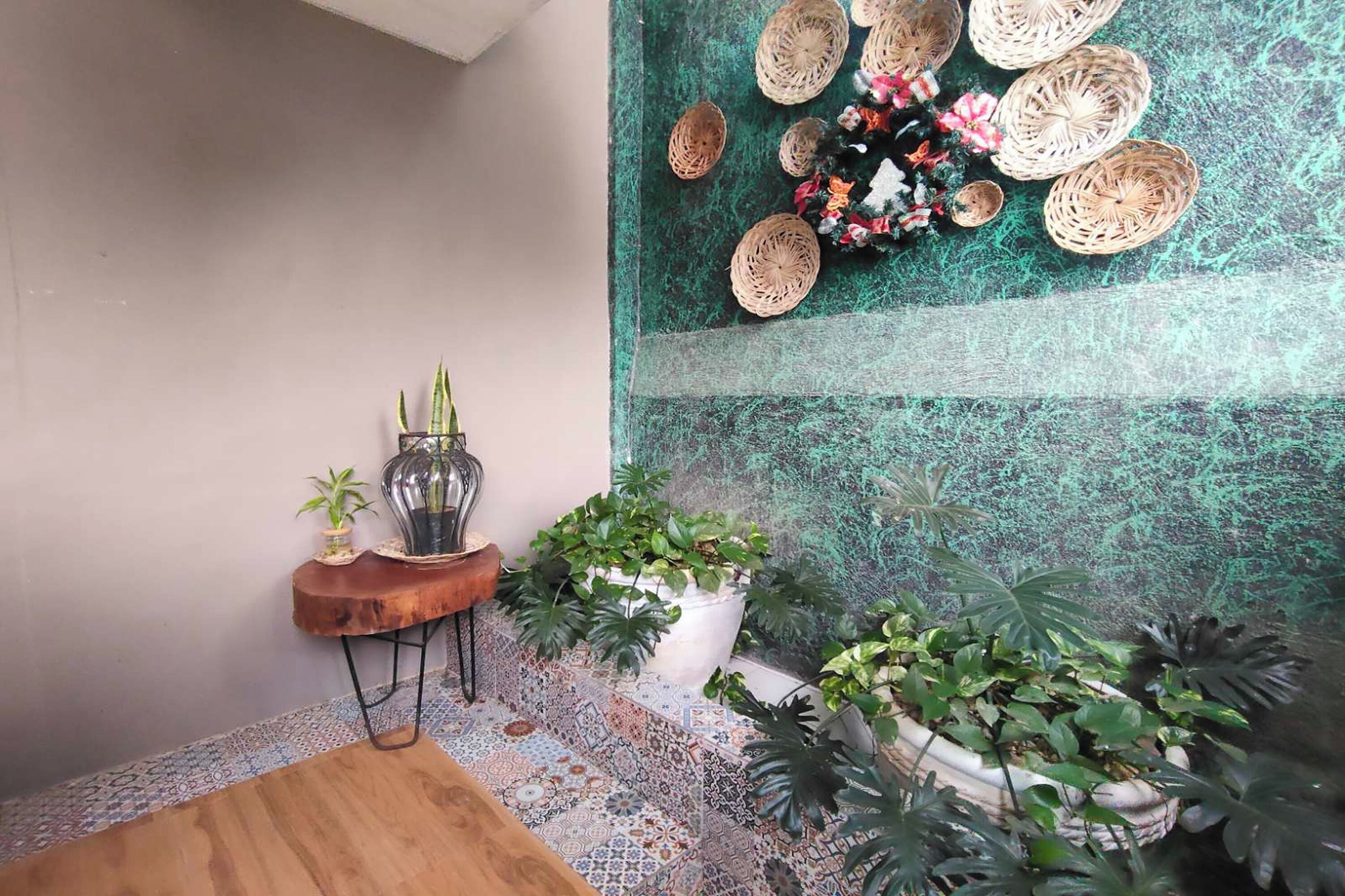 Un coin aménagé avec une table en bois, une petite table d’appoint ornée d’un vase et d’une plante, et un mur décoré de paniers tressés et de plantes en pot.