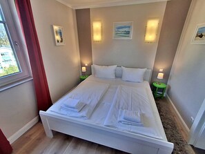 Un lit double bien fait, avec du linge de lit blanc, deux tables de chevet avec des lampes et des tableaux encadrés accrochés aux murs.