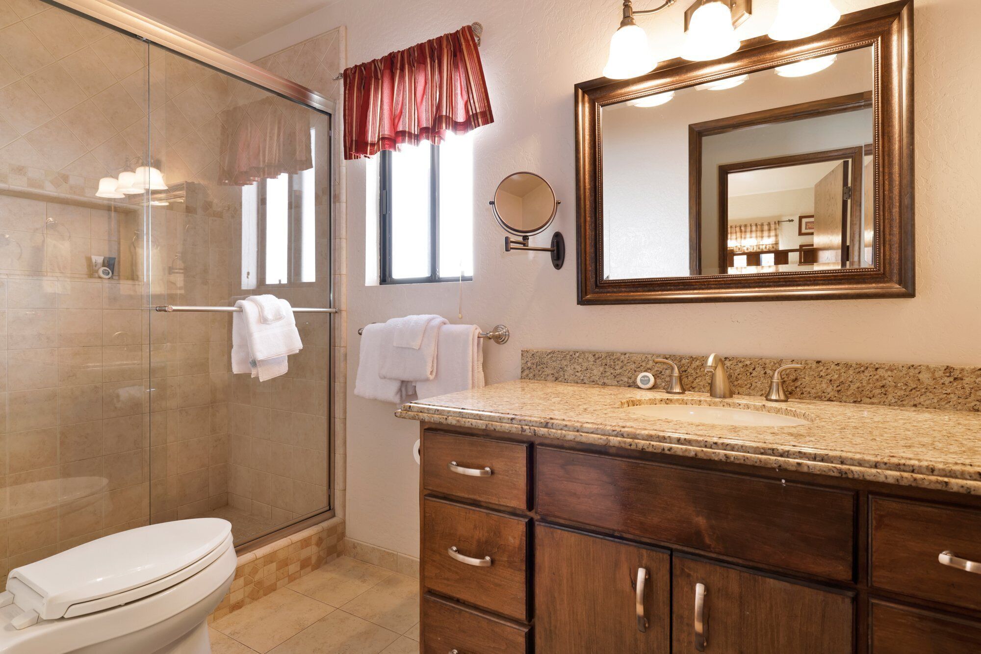 A bathroom with a glass shower, a sink with a granite countertop, and a large mirror above the sink.