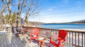 A wooden deck with a table and chairs, overlooking a lake with a clear view of the surrounding landscape. - Shore Acres Lodge #452 (Big Bear Lake)
