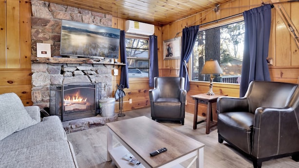 A cozy cabin interior with a stone fireplace, leather chairs, a wooden ceiling, and a window with curtains. - Shore Acres Lodge #452 (Big Bear Lake)
