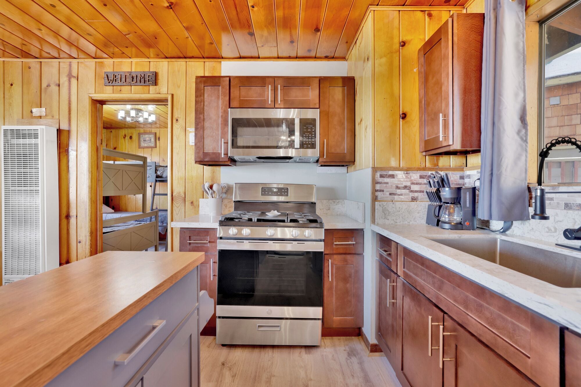A compact kitchen with wooden cabinets, a microwave, a stove, and a coffee maker.