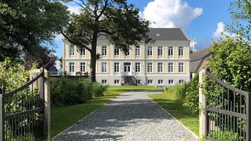 Ein großes, mehrstöckiges Gebäude mit einer symmetrischen Fassade, einer zentralen Treppe und einem Kiesweg zum Eingang.