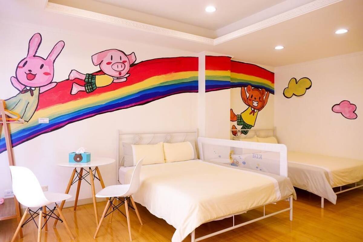 A children's room with a bed, two single beds, a small table, and chairs.