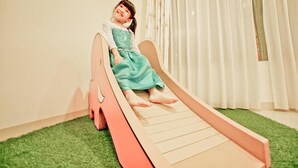 A child sitting on a slide in a room with a green carpet and white curtains. - Kid Baby Homestay (Tainan)