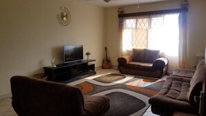 A living room with a flat-screen TV, a guitar, and two sofas. - Belle Ocean View Apartments (Mombasa)
