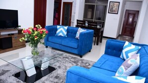 A living room with a blue sofa, a glass coffee table, and a vase of flowers. - Belle Ocean View Apartments (Mombasa)
