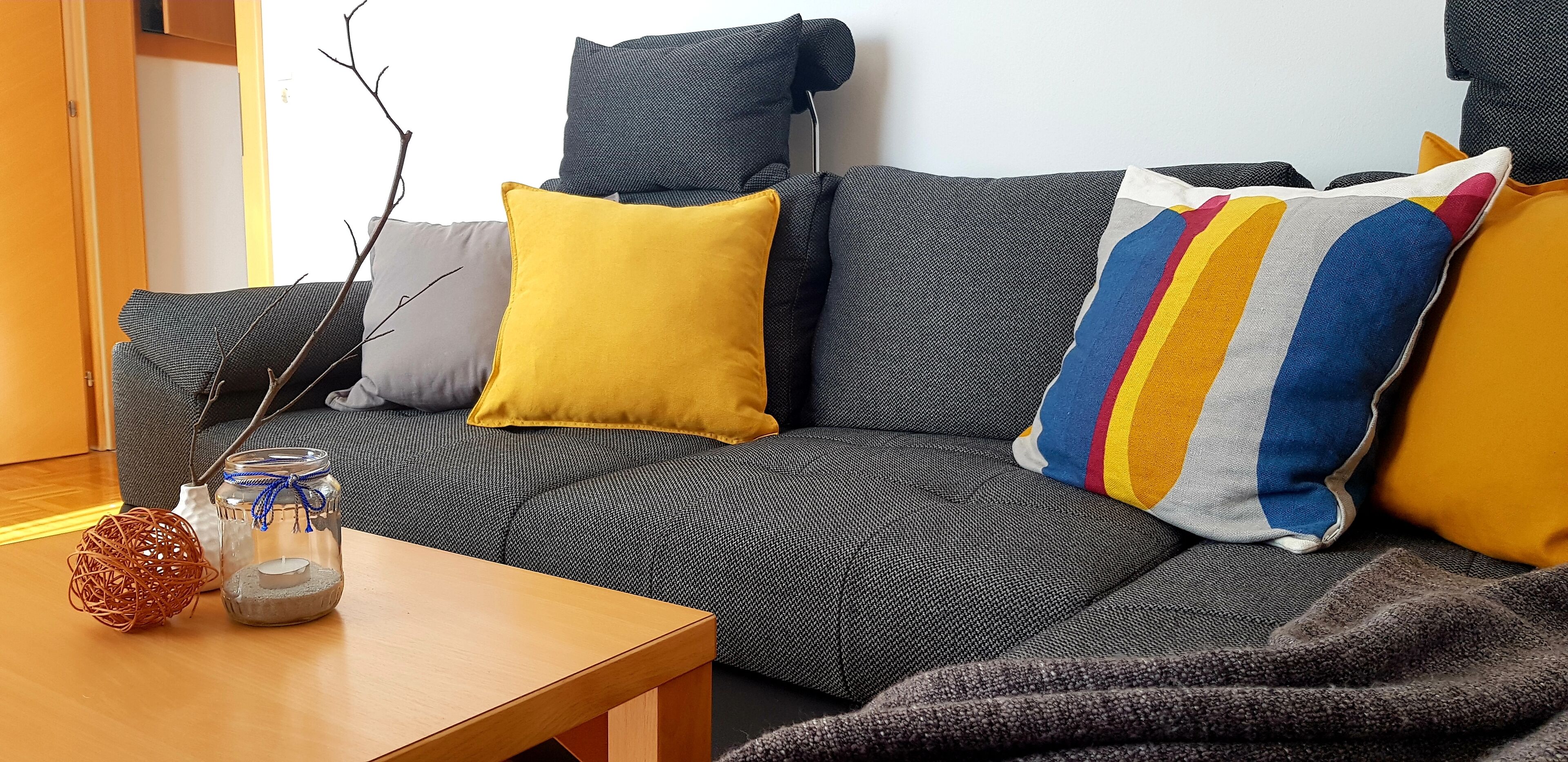 A modern living room with a grey sofa, a wooden coffee table, and a vase with a candle.