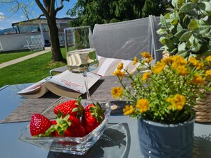 A table with a book, a glass of white wine, a bowl of strawberries, and a potted plant with yellow flowers. - Ferienpark Scheiber (Sankt Kanzian am Klopeiner See)