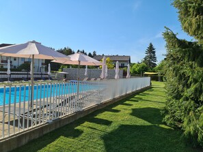 A swimming pool with lounge chairs and umbrellas, surrounded by a white fence and a well-maintained lawn. - Ferienpark Scheiber (Sankt Kanzian am Klopeiner See)