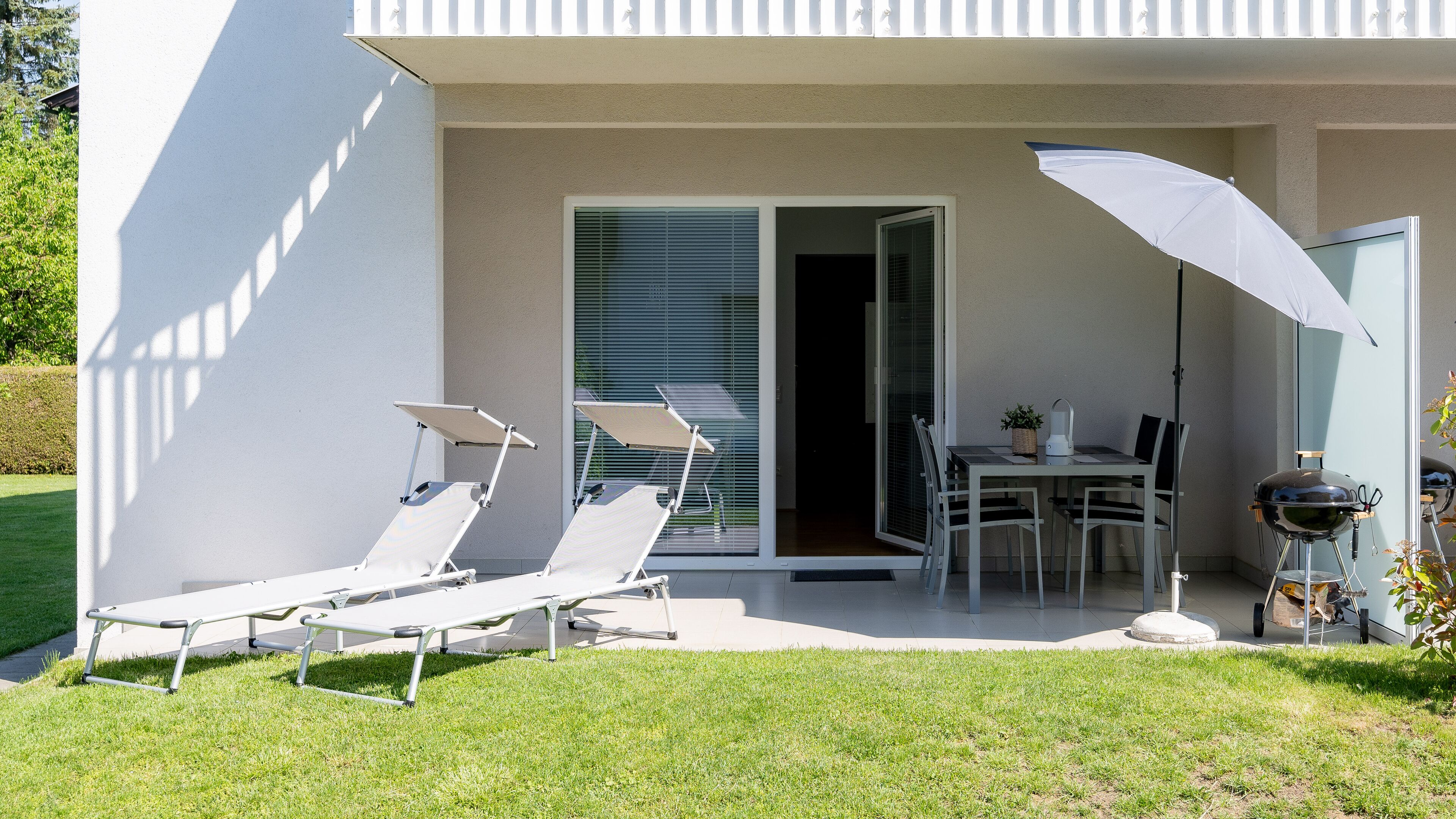 A modern outdoor patio with a dining table, chairs, and a grill.