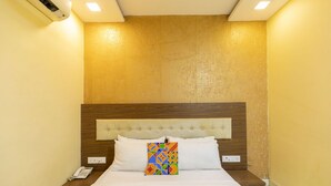 A hotel room with a wooden headboard, a bed with white linens, a colorful geometric pillow, and a bedside phone. - Hotel Elite 59 (Mumbai)