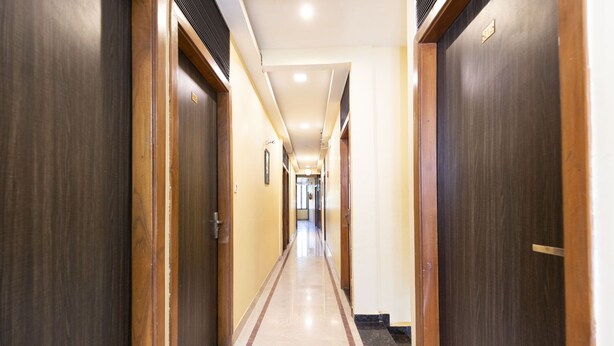 A hotel corridor with wooden doors, a tiled floor, and a ceiling with recessed lighting. - Hotel Elite 59 (Mumbai)