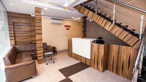 A reception area with a wooden reception desk, a sofa, and a staircase. - Hotel Elite 59 (Mumbai)