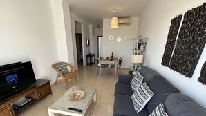 A living room with a sofa, a coffee table, a TV, and a dining area with a table and chairs. - Nerja Paradise Rentals - Apartment Chimenea C1D (Nerja)