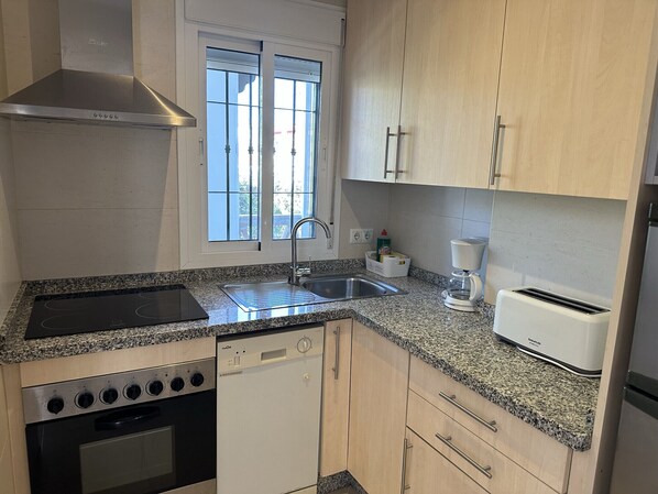Una cocina compacta equipada con estufa, horno, lavavajillas, pileta y cafetera.