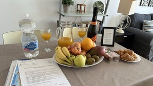 A breakfast table with a bottle of water, juice glasses, a bottle of wine, a plate of fruits, and pastries. - Nerja Paradise Rentals - Apartment Chimenea C1D (Nerja)