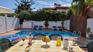 A poolside dining area with a table set for two, a pool, and lounge chairs. - Nerja Paradise Rentals - Villa Kaisaras (Nerja)