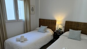 Una habitación de hotel con dos camas individuales, una mesita de noche con lámpara, una obra de arte en la pared y una ventana con cortinas.
