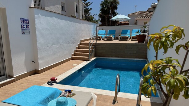 Una piscina con sillas reclinables, una pequeña escalera y un cartel en la pared.