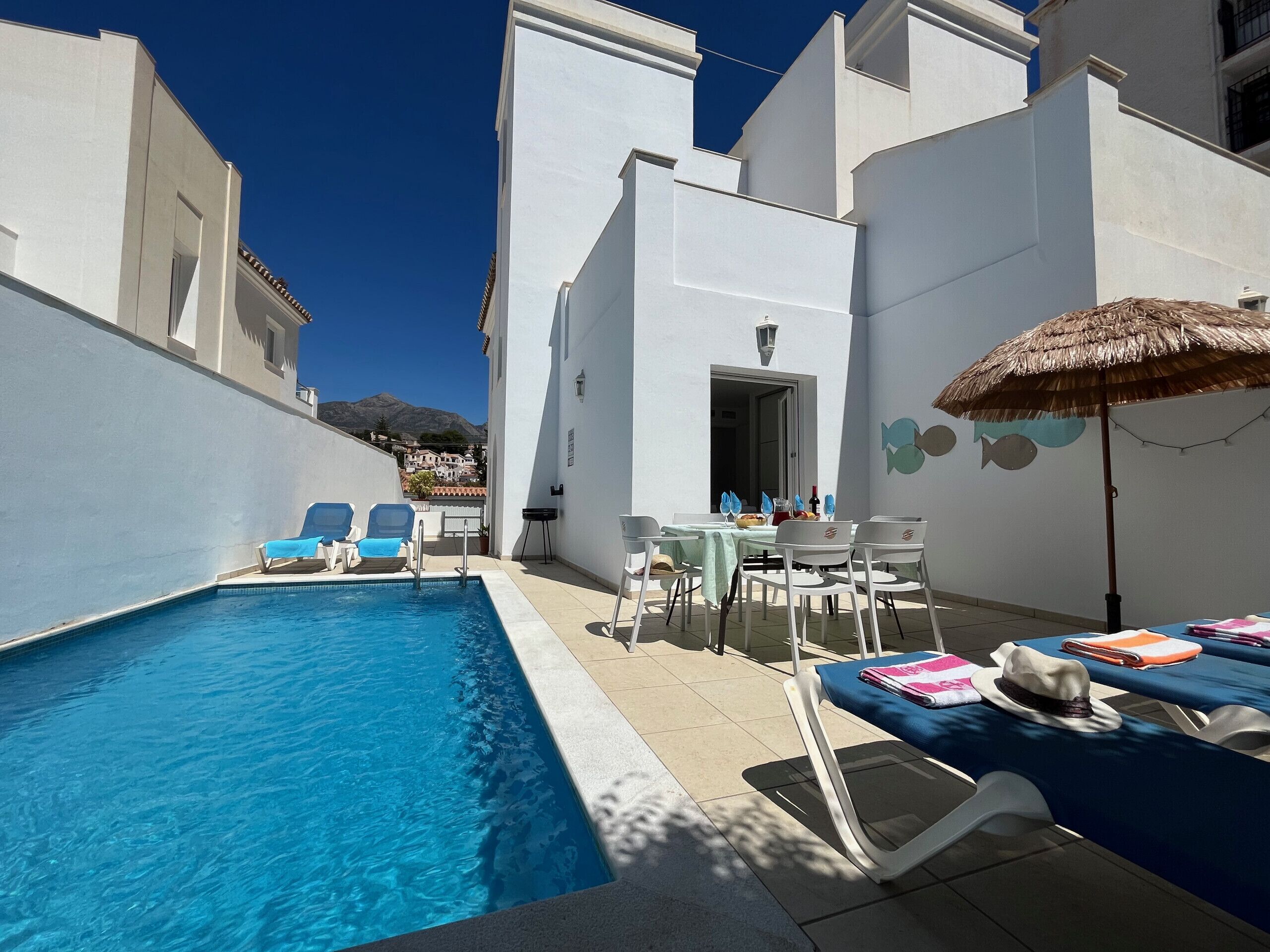 Ein Poolbereich mit Liegestühlen, einem Tisch mit Tischdecke und einem Reetdachschirm.
