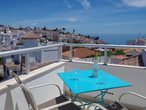 Un balcon avec une table bleue, deux chaises et une bouteille d’eau.